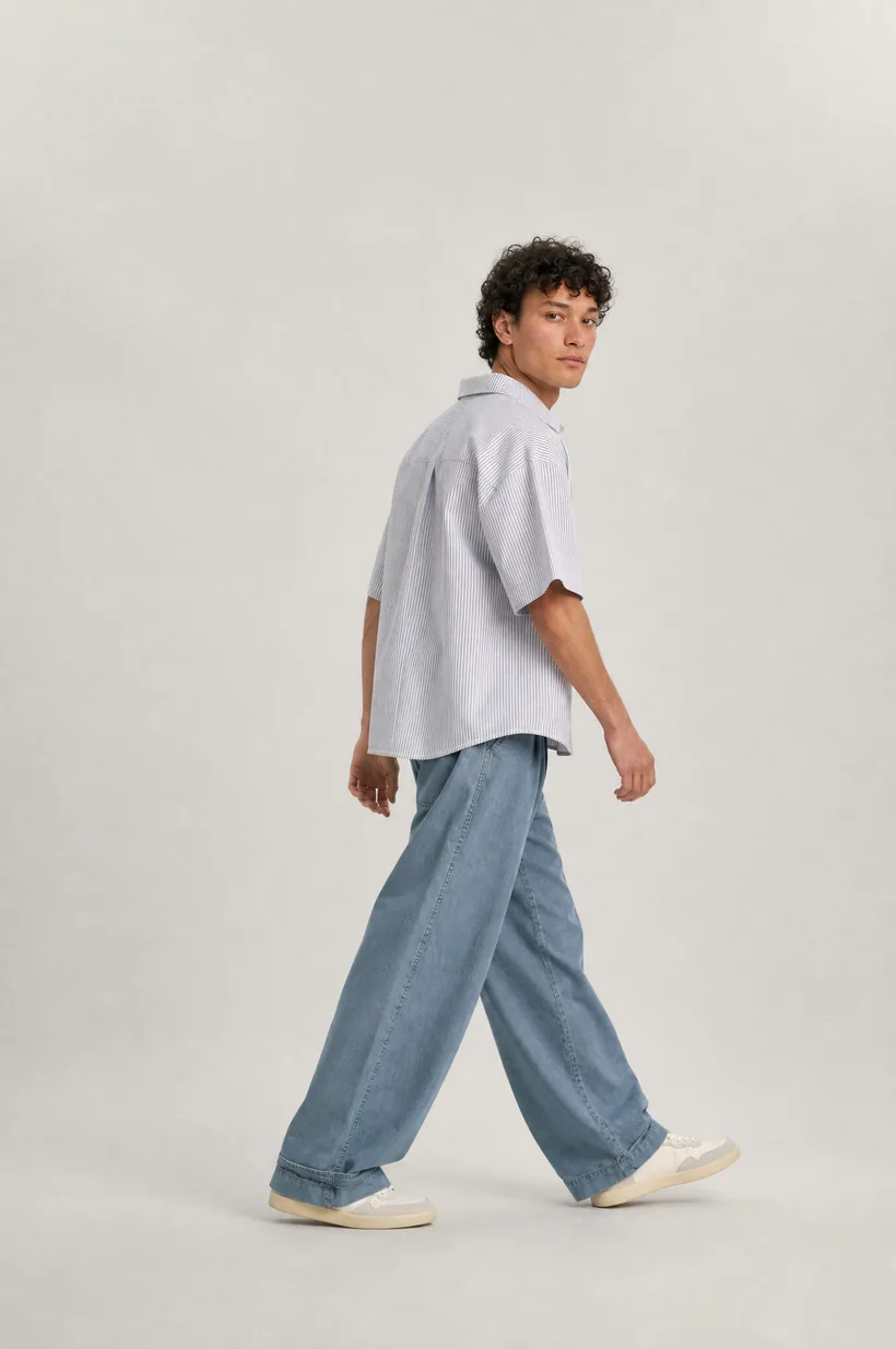 Modelo de perfil caminando con polo claro y jean ancho