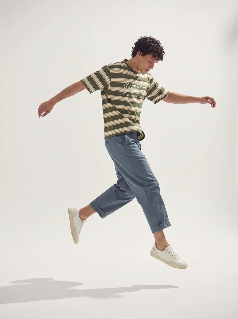 Modelo en salto con remera de rayas verdes y pantalón azul
